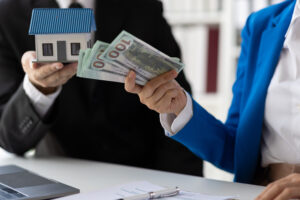 Person exchanging cash to collect rent payments while holding a model house.