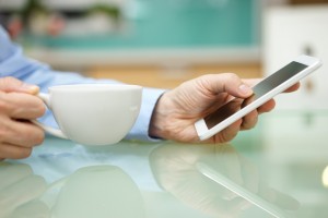 man is using smart mobile phone and drinking coffee at home